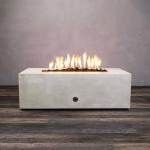 A white concrete Starfire Designs Gravity 48" x 32" Rectangle Gas Fire Pit with bright flames rising from the linear burner. The modern design contrasts with the gray backdrop, showcasing the fire pit's sleek look. Ideal for outdoor settings, this fire pit is built with durable materials, making it suitable for any weather.