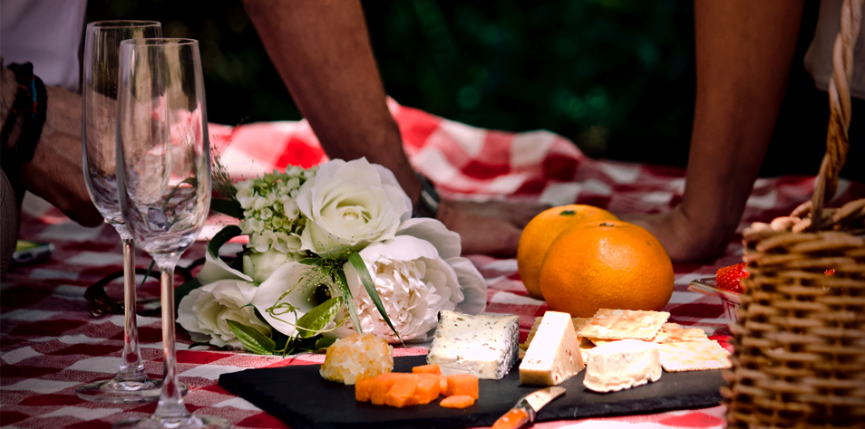 picnive with 2 champagne glasses and some flowers and vegetables over a picnic blanket