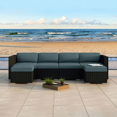 A wicker patio sectional set with turqouis fabric matches the afternoon sunset of the beach behind it.