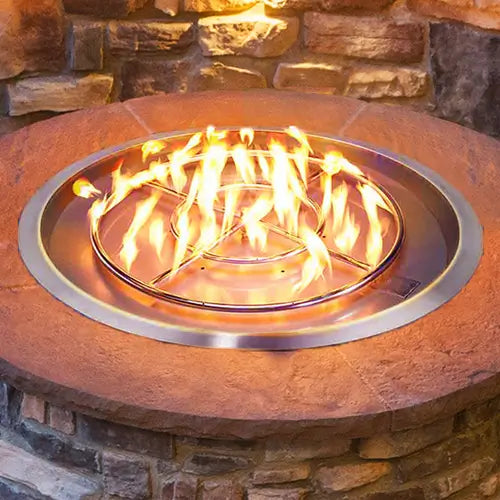 A stainless steel gas burner pan and ring is ignited in an outdoor DIY fire pit setup closeup