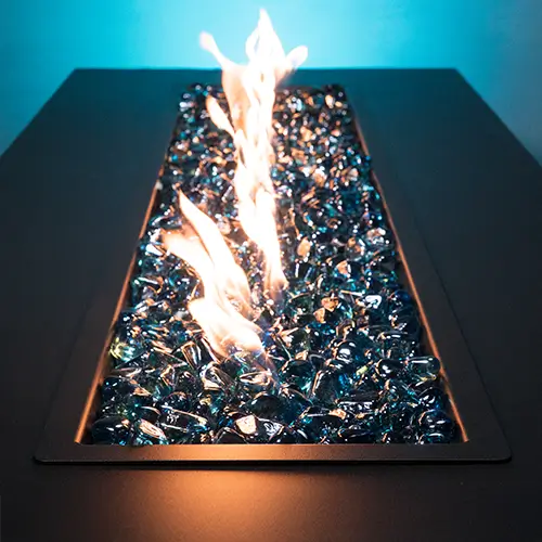 Stunning cobalt blue fire glass rests in the center of a modern black fire pit backlit with matching blue haze.
