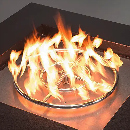 A gas fire pit ring burner is ablaze in the middle of a modern copper tone fire pit.