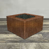 A side view of the 36" Square Gravity Corten Steel Fire Pit by Starfire Designs - perfect for outdoor patio spaces. Natural gas or propane compatible, enhancing warmth and ambiance. Lava rocks included for added aesthetic.