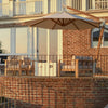 Cozy elevated brick patio featuring the 42-Inch Square Beton Concrete GFRC Gas Fire Pit in White by Starfire Designs, seamlessly integrated with plush cushioned seating and a cantilever umbrella / captured at golden hour, perfect for stylish and relaxing outdoor moments.