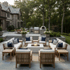 A spacious stone patio features a large U-shaped seating arrangement surrounding a white patio fire pit. The setting is framed by a grand stone residence and an outdoor kitchen, creating a perfect family gathering fire pit area. The steady flame of the outdoor fire pit serves as a warm focal point, with the fire table anchoring the elegant garden furniture.