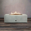 A low, light gray concrete fire pit with a clean rectangular shape burns in a narrow line of golden flames above smooth lava rocks, the modern fire pit centered on a wide plank floor against a plain gray wall, and the GIF loops as the gas fire pit quietly flickers, emphasizing the long opening, crisp edges, and minimalist profile of this rectangular fire pit in a simple studio setting.