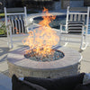 Inviting outdoor fire pit scene featuring a round stone fire pit filled with shimmering reflective fire glass, producing vibrant flames. Surrounded by white rocking chairs with striped pillows and positioned near a serene backyard pool, this setup offers the perfect mix of warmth, comfort, and style—available at starfiredirecv.com.