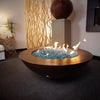 54-inch Copa Moreno copper fire pit by Starfire Designs, beautifully displayed indoors with glowing blue fire glass, highlighting the fire pit's luxurious hand-hammered copper finish
