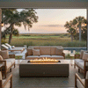 A soft beige sofa and matching armchairs are arranged in a U-shape around a low concrete fire pit on a covered terrace, the slim rectangular burner producing a bright, continuous line of flame as it reflects off nearby pool water and the marshy coastal landscape beyond, creating a sheltered patio fire pit nook that reads as a cozy backyard fire pit and versatile outdoor fire pit lounge for quiet sunset views and conversation.
