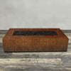 A side view of the 72" x 38" Rectangle Gravity Corten Steel Fire Pit by Starfire Designs - perfect for outdoor patio spaces. Natural gas or propane compatible, enhancing warmth and ambiance. Lava rocks included for added aesthetic.