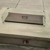Outdoor fire feature with an oil rubbed bronze linear burner cover by American Fire Products, enclosed in a tempered glass wind guard atop a concrete base—blending durability, style, and safety in a modern patio setting.