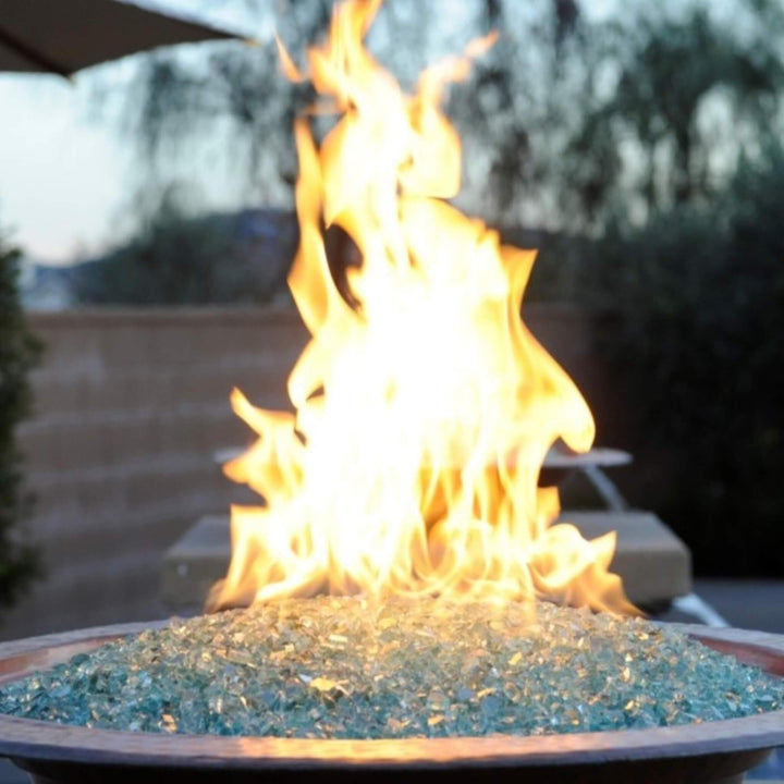 Close-up of vibrant flames rising from a copper fire bowl filled with American Fire Products 1/4" Non-Reflective Classic Fire Glass in light aqua, showcasing a clean, contemporary fire feature perfect for upscale outdoor spaces.