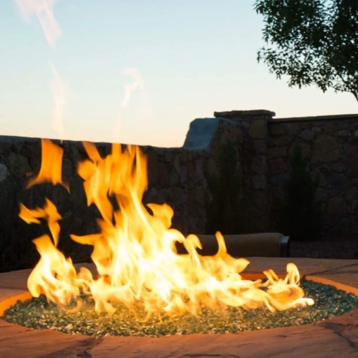 Vibrant backyard fire feature glowing with American Fire Products 1/4" Non-Reflective Classic Fire Glass, set into a stone fire pit and dancing with tall flames at sunset—ideal for creating a cozy and elegant outdoor atmosphere.