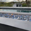Close-up of a modern rectangular fire pit filled with American Fire Glass 1/2" Maui Breeze pre-mixed fire glass, featuring a sparkling blend of sky blue, cobalt, and silver tones. Set beside a tranquil pool with scenic views, this setup captures the essence of outdoor relaxation and upscale ambiance—available now at starfiredirecv.com.