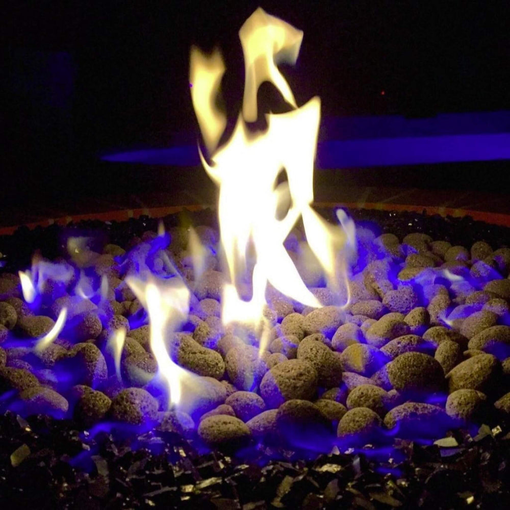 Close-up nighttime view of American Fire Products Small Gray Lava Stones glowing under mesmerizing blue and yellow flames, creating a dramatic and cozy ambiance in a fire pit enhanced with black fire glass.