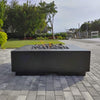 Modern black fire table topped with American Fire Products Small Gray Lava Stones, set against a waterfront patio with lush greenery—offering a clean, coastal outdoor ambiance with a touch of flame-driven elegance.