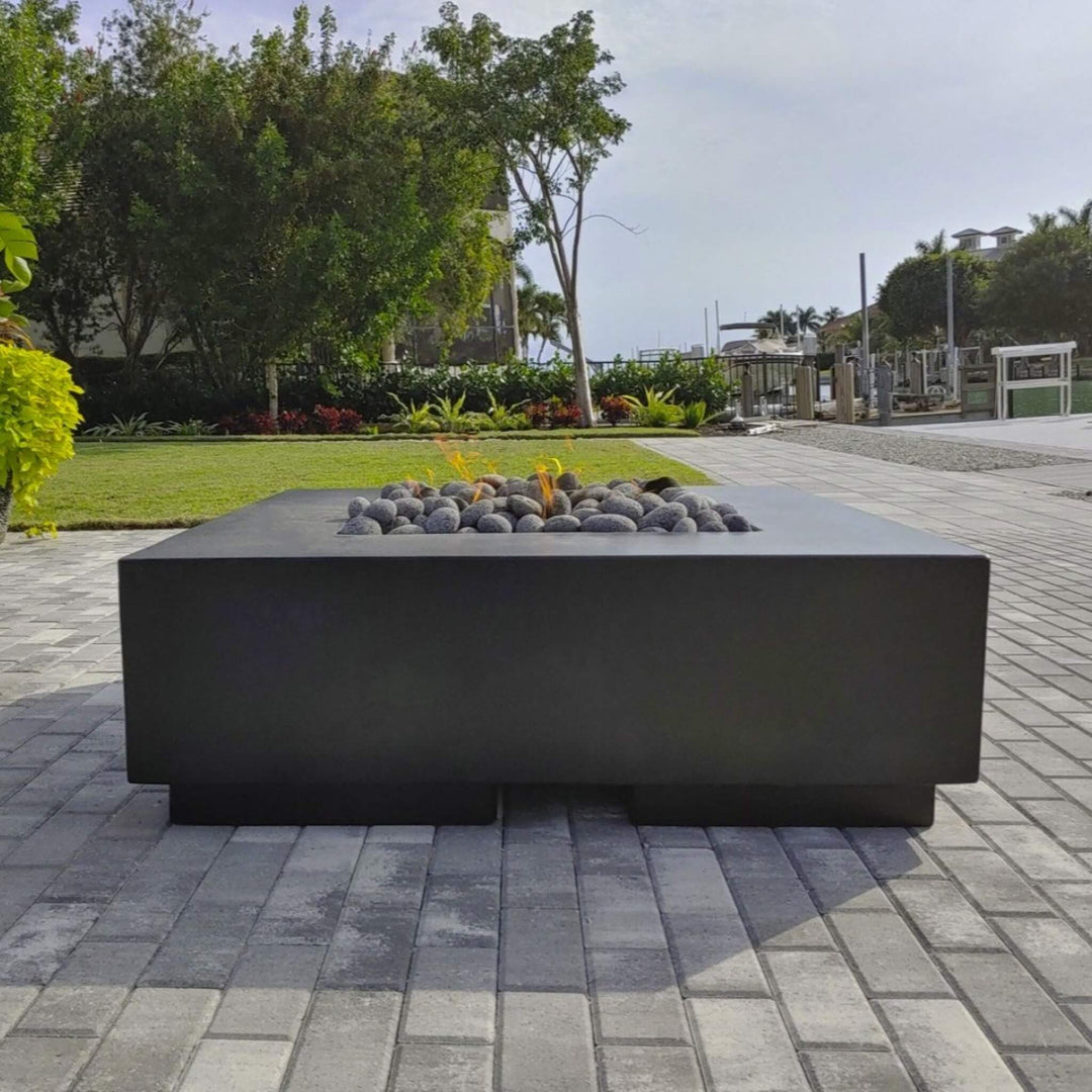 Modern black fire table topped with American Fire Products Small Gray Lava Stones, set against a waterfront patio with lush greenery—offering a clean, coastal outdoor ambiance with a touch of flame-driven elegance.
