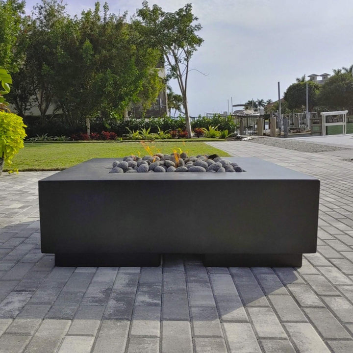 Modern black fire table topped with American Fire Products Small Gray Lava Stones, set against a waterfront patio with lush greenery—offering a clean, coastal outdoor ambiance with a touch of flame-driven elegance.