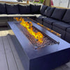 Contemporary outdoor fire table filled with American Fire Products Small Gray Lava Stones, framed by a sleek glass wind guard and warm flames, set beside a modern black wicker sectional on a wood deck—perfect for upscale backyard lounging.