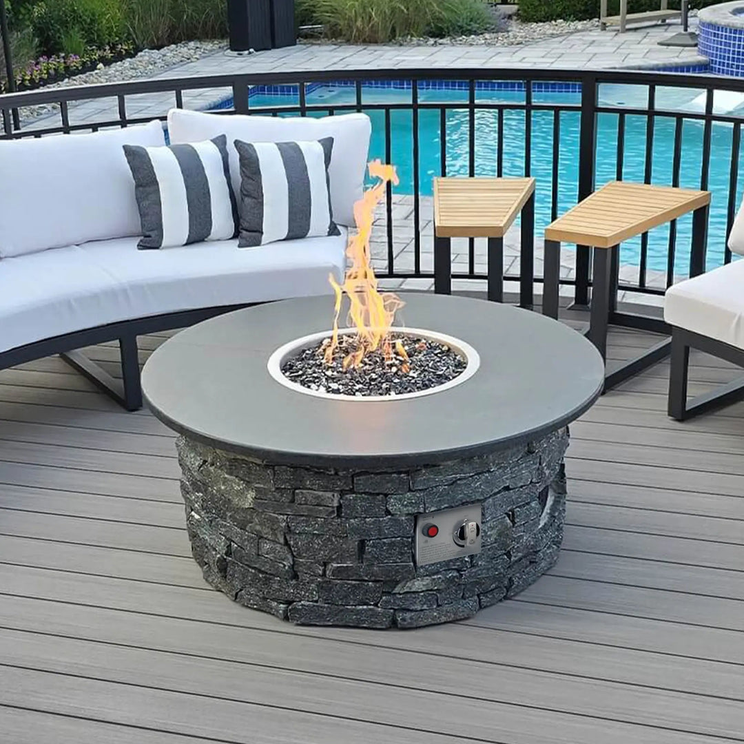 A stylish backyard fire pit setup featuring a round stone fire pit with a smooth modern top, centered around a bright flame fueled by an American Fire Products stainless steel drop-in kit. This CSA-certified system ensures safety while showcasing reflective fire glass. Surrounded by cozy white patio seating and set beside a sparkling pool, the scene blends relaxation, safety, and modern design for the perfect outdoor gathering space.