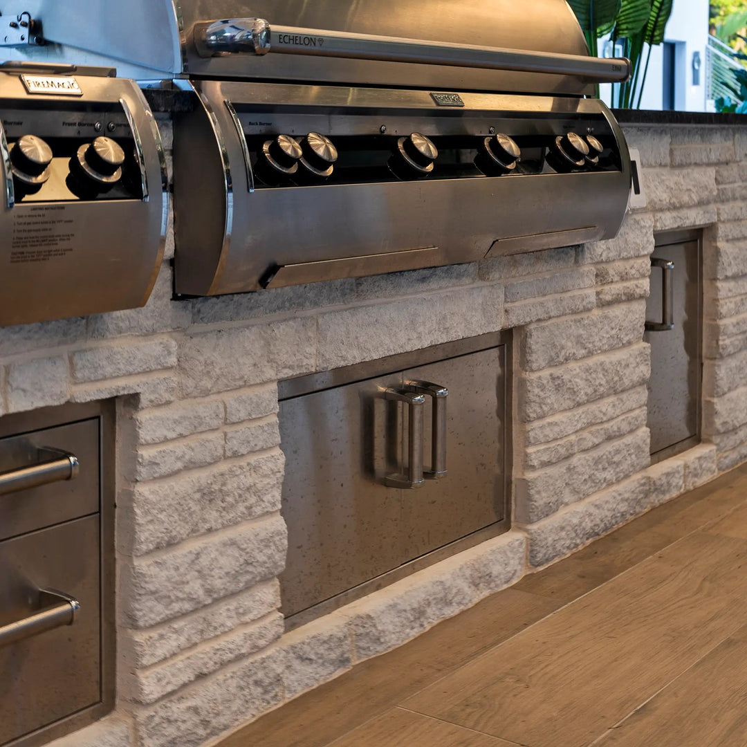 A Fire Magic Premium Double Doors with Trash Tray and Dual Drawers isntalled underneath the outdoor kitchen of a modern patio with an enormous Fire Magic Grill above it.