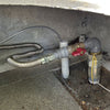 Detailed view of an outdoor gas line setup with a corrugated stainless steel hose, connected to a shut-off valve and various fittings under a patio, ensuring safe gas flow control