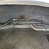 Close-up view of an outdoor gas line installation with corrugated stainless steel hoses connected to secure fittings under a patio, highlighting a safe and stable gas connection setup