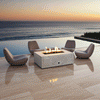 Four modern sculptural chairs surround a white luxury fire pit on a polished stone terrace overlooking the ocean at sunset. The reflection of the fire feature is visible on the glossy floor, adding depth to the scene. The steady amber flames of the propane fire pit create a focal point for outdoor entertaining, blending with the golden hues of the sky and the deep blue water.