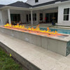 Modern outdoor living space with a long poolside fire feature illuminated by the HPC Fire Inspired Linear Flat Torpedo T-Burner, creating a warm and inviting nighttime atmosphere.