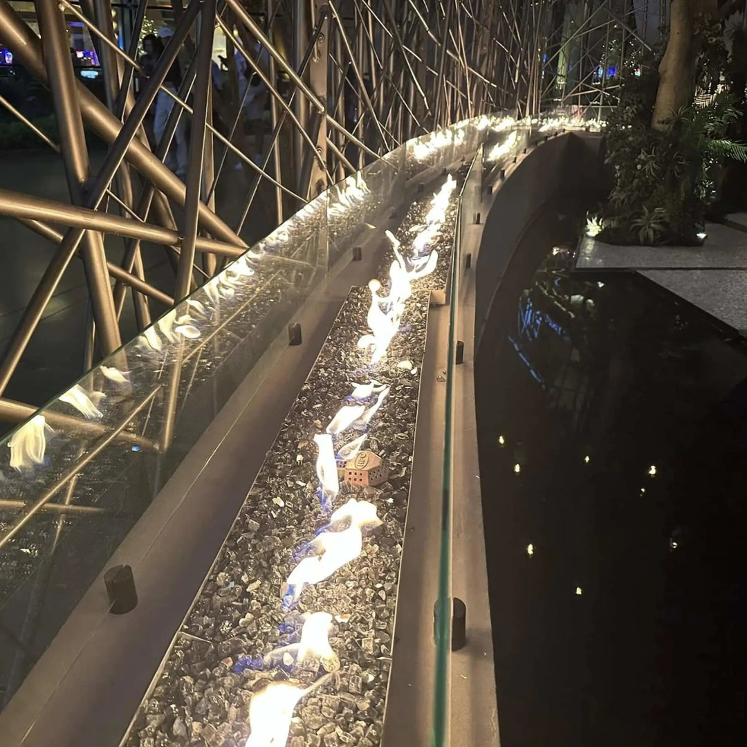 Long curved commercial fire feature with bright orange flames reflecting off black crushed glass, powered by the HPC Fire Inspired Linear Interlink Torpedo T-Burner for an elegant modern design.