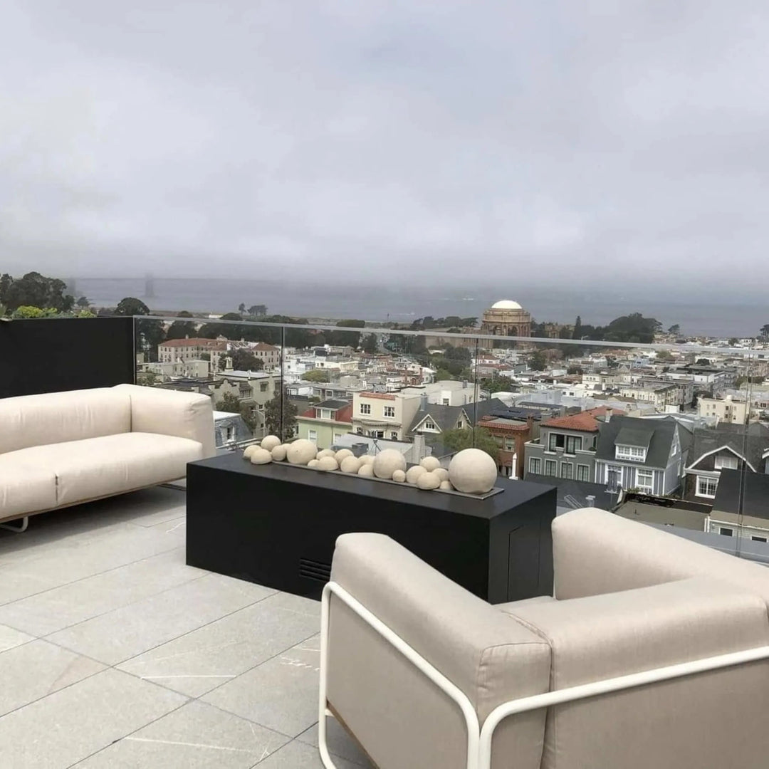Elegant rooftop patio with a black rectangular fire feature filled with decorative spheres, offering a panoramic view of the city, highlighting the modern style of the HPC Fire Inspired Torpedo T-Burner in a linear trough design.