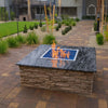 Outdoor fire feature set in a stone-top pit with a Square Drop-In Penta Burner by HPC Fire, producing lively flames over cobalt blue fire glass—perfect for upscale residential landscapes.
