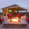 Backyard bar and lounge area glowing with the ambiance of a stone-built square fire pit, lit with bold flames from an HPC certified flat burner / perfect for game night gatherings and outdoor entertaining.