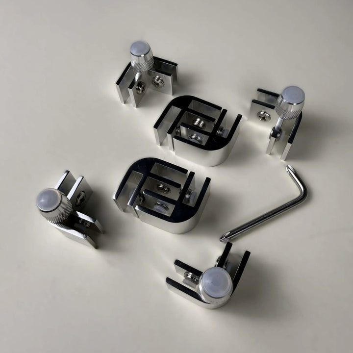 Top view of the Starfire Designs Béton Fire Pit Replacement Glass Wind Guard Clips Kit featuring precision-milled L-shaped clips, mounting hardware, and adjustment tools for rectangular or square guards.