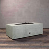 A side view of the Starfire Designs Gravity 48" x 32" Rectangle Rustic Gravity Concrete (GFRC) Fire Pit - Propane Gas Hardline - Natural Gray with flames on, featuring sleek modern concrete bowl design and durable construction, perfect for outdoor patio spaces. Natural gas or propane compatible, enhancing warmth and ambiance. Lava rocks included for added aesthetic.
