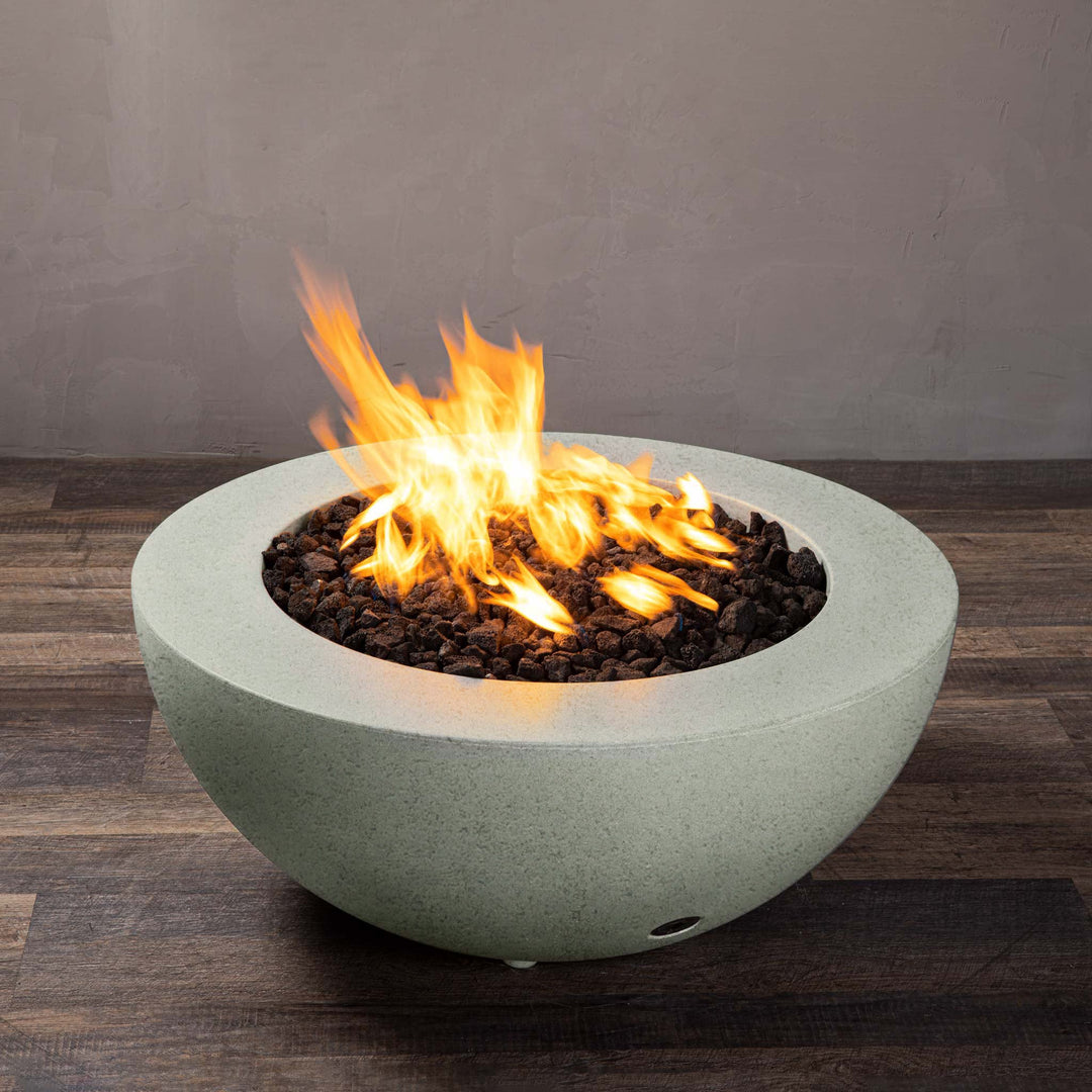 A side view of the Starfire Designs Gravity 36" Round Rustic Gravity Concrete (GFRC) Fire Pit - Propane Gas Hardline - Natural Gray with flames on, featuring sleek modern concrete bowl design and durable construction, perfect for outdoor patio spaces. Natural gas or propane compatible, enhancing warmth and ambiance. Lava rocks included for added aesthetic.
