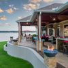 Gray Sedona Fire Bowls by The Outdoor Plus with blue fire glass, neatly positioned on stone columns across a lakefront patio, delivering breathtaking views and glowing warmth.