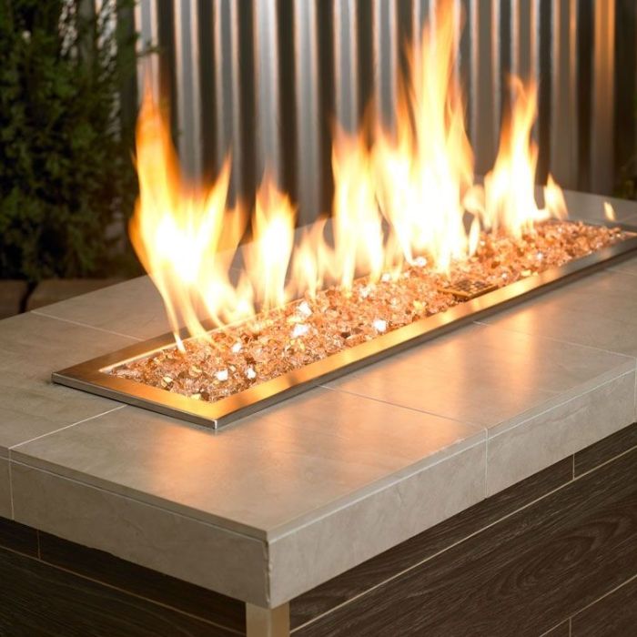 Champagne-colored 1/4" reflective fire glass by American Fire Products shown glowing beneath a lively flame in a sleek, modern fire feature—adding a warm, golden shimmer and luxurious ambiance to this outdoor setting.