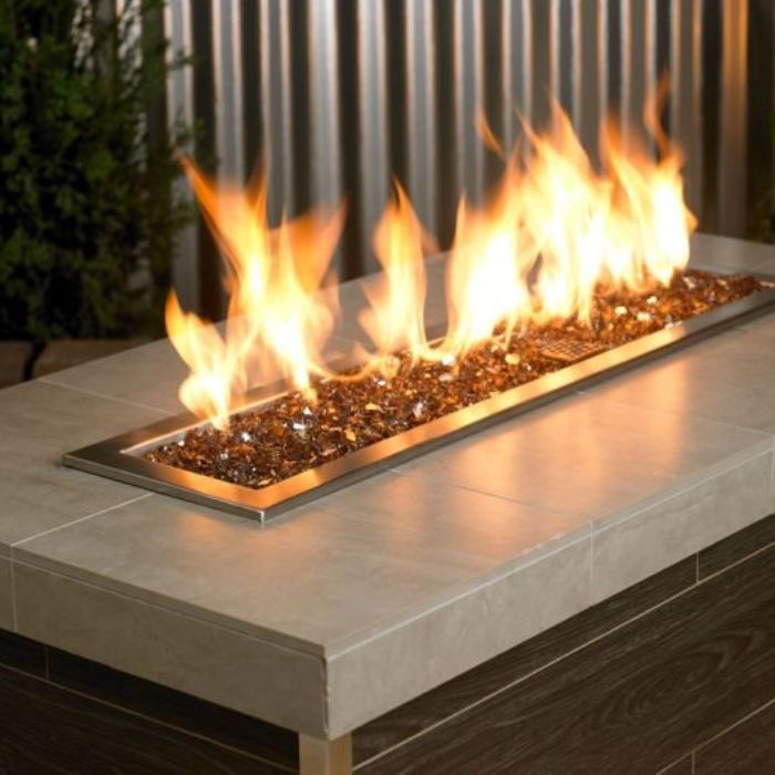 Warm copper-toned 1/4" reflective fire glass by American Fire Products showcased in a sleek linear fire feature, with golden flames dancing above the sparkling glass—perfect for adding rich, earthy elegance to any modern outdoor setting.