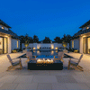 A symmetrical backyard fire pit area features a rectangular concrete fire pit positioned before a long swimming pool under a deep blue evening sky. Four wooden Adirondack chairs face the central fire feature, where steady flames burn cleanly, illustrating the benefits of a smokeless fire pit. The scene highlights the architectural balance and warm lighting of a modern residential courtyard at night.