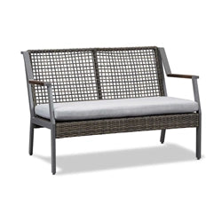 A stylish outdoor loveseat featuring a sleek metal frame with woven rattan detailing and plush light gray cushions. The loveseat offers a modern yet comfortable seating option for outdoor patios, blending durability with contemporary design.