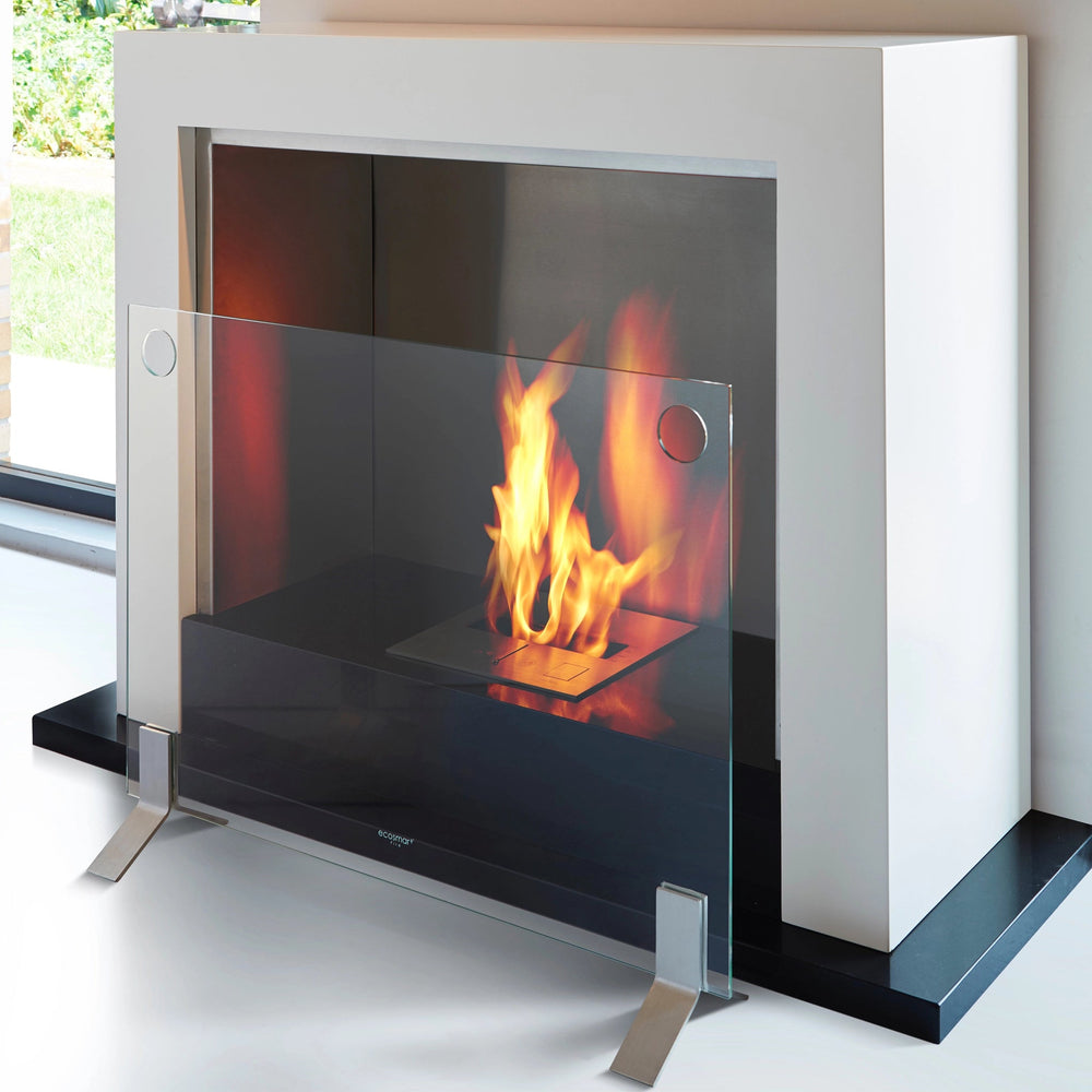 The EcoSmart Fire Plasma Glass Fire Screen is displayed in use, complementing a modern bioethanol fireplace. Featuring a transparent tempered glass panel with stylish stainless steel feet, this freestanding fire screen provides essential protection while maintaining an open, sophisticated aesthetic. Designed for safety and elegance, it enhances any contemporary indoor fireplace setting. fireplace safety screen, modern glass fire barrier, tempered glass fireplace guard, eco-friendly fire protection.