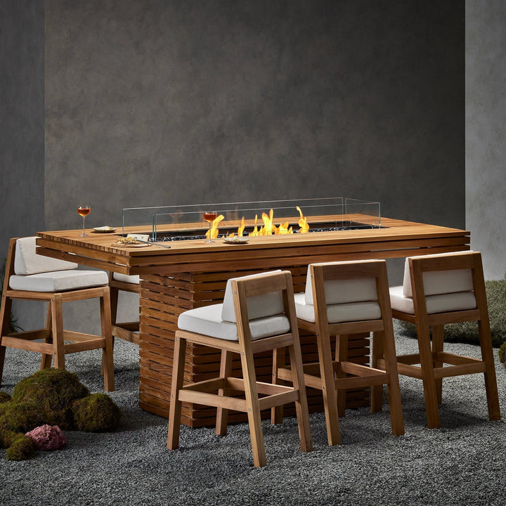 The EcoSmart Fire Gin 90 (Bar) Teak Fire Pit is elegantly integrated into a contemporary indoor dining setting, surrounded by high-end seating and warm lighting. This luxury fire pit table doubles as a centerpiece for stylish restaurant interiors, offering a freestanding gas fire pit option that blends seamlessly with modern dÃ©cor. The natural gas fire pit ensures efficient heating and a mesmerizing flame display.