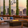The EcoSmart Fire Gin 90 Chat Height outdoor fire table enhances a contemporary rooftop lounge, featuring comfortable patio seating, decorative lighting, and lush greenery. This rectangular gas fire pit with a glass wind guard offers a luxurious atmosphere for entertaining. Designed with high-quality materials, this modern fire table is ideal for commercial patios, high-end outdoor lounges, and backyard spaces.