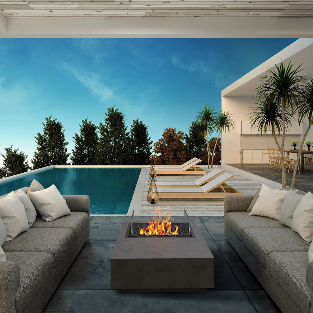 A contemporary outdoor gas fire table setup with the EcoSmart Fire Manhattan 50, positioned beside an infinity pool and surrounded by modern seating. The sleek concrete design and fire bowl outdoor fire pit style make it an elegant addition to luxury fire pits in high-end outdoor spaces, providing warmth and ambiance for stylish evenings.