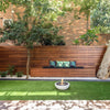 The EcoSmart Fire Mix 600 Bone Fire Pit is featured in an elegant outdoor patio setting, placed on a lush green lawn with a wooden bench and decorative pillows in the background. This modern fire pit bowl is filled with black lava rocks and emits a warm, inviting flame, making it the perfect centerpiece for any backyard fire pit arrangement. Designed for both aesthetics and functionality, it provides an eco-friendly fire pit outdoor experience.