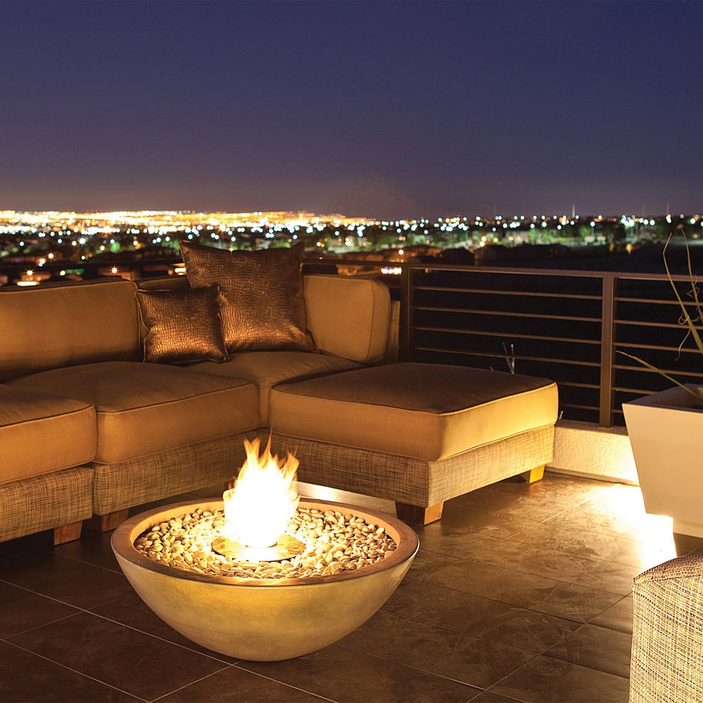 A stunning EcoSmart Fire Mix 850 natural fire pit on a high-end rooftop lounge, providing warmth and ambiance against a scenic city skyline. The round concrete fire pit is filled with natural stone fire media, creating a striking focal point for luxury outdoor seating areas and contemporary fire tables.