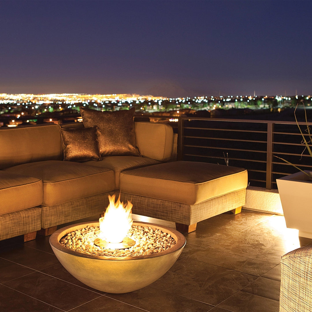 A stunning EcoSmart Fire Mix 850 natural fire pit on a high-end rooftop lounge, providing warmth and ambiance against a scenic city skyline. The round concrete fire pit is filled with natural stone fire media, creating a striking focal point for luxury outdoor seating areas and contemporary fire tables.