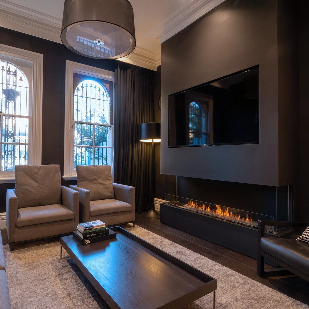 Modern luxury living room with a sleek linear fireplace under a wall-mounted TV, featuring dark walls, grey armchairs, minimalist coffee table, and large arched windows with wrought iron details, creating a sophisticated and cozy atmosphere