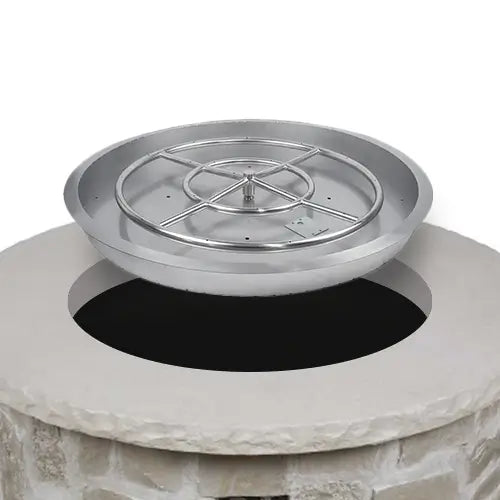 A fire pit drop-in burner system for a DIY setup is being placed into a stone fire pit setup to complete the project on a white background